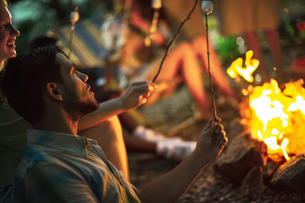 Young couple roasting marshmallows over bonfire.
