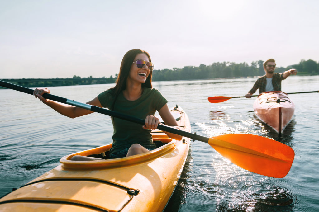 Two young people kayaking on lake together and smiling.