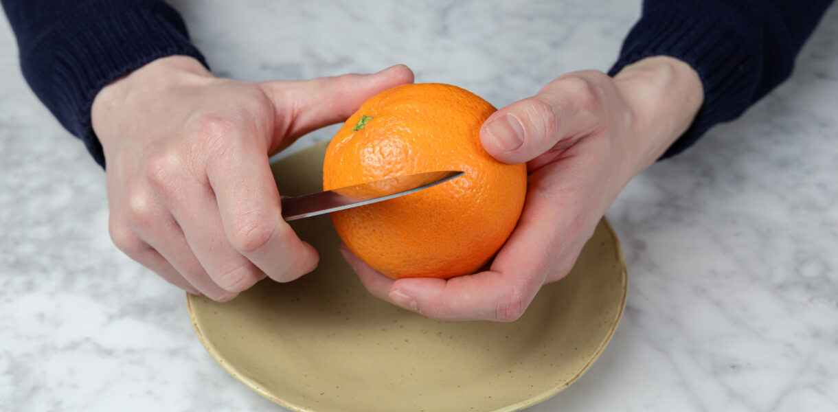 Pair of hands holding an orange, beginning to peel it.