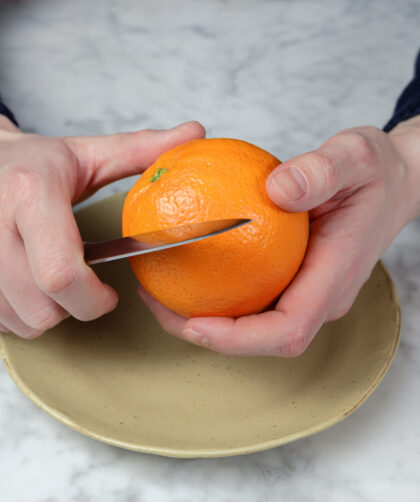 Pair of hands holding an orange, beginning to peel it.