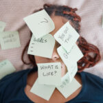 Woman laying in bed with her face covered in sticky notes questioning life