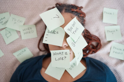 Woman laying in bed with her face covered in sticky notes questioning life