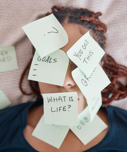 Woman laying in bed with her face covered in sticky notes questioning life