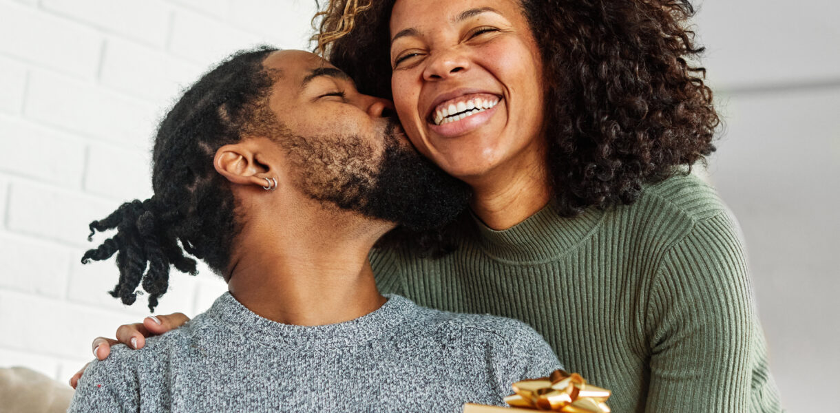 Young woman giving her boyfriend a present as he kisses her cheek in appreciation