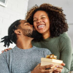 Young woman giving her boyfriend a present as he kisses her cheek in appreciation