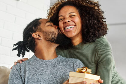 Young woman giving her boyfriend a present as he kisses her cheek in appreciation