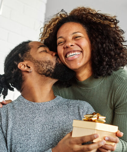 Young woman giving her boyfriend a present as he kisses her cheek in appreciation