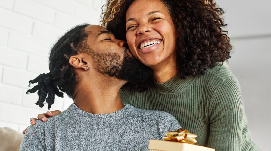 Young woman giving her boyfriend a present as he kisses her cheek in appreciation