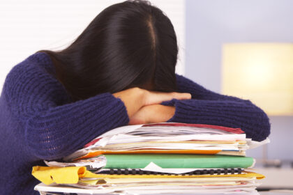 woman with long, dark hair with head down on top of a pile of folders and books