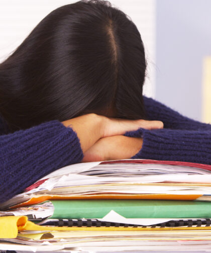 woman with long, dark hair with head down on top of a pile of folders and books