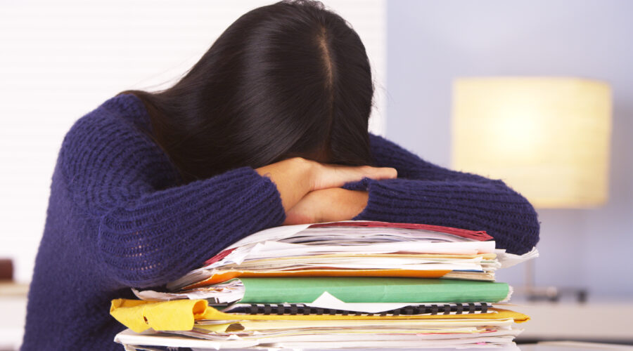 woman with long, dark hair with head down on top of a pile of folders and books