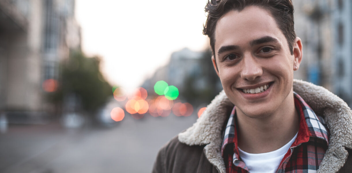 Waist up portrait of delighted young male standing on street and smiling. He is happy to walk on his own. Copy space in left side
