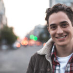 Waist up portrait of delighted young male standing on street and smiling. He is happy to walk on his own. Copy space in left side