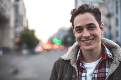 Waist up portrait of delighted young male standing on street and smiling. He is happy to walk on his own. Copy space in left side