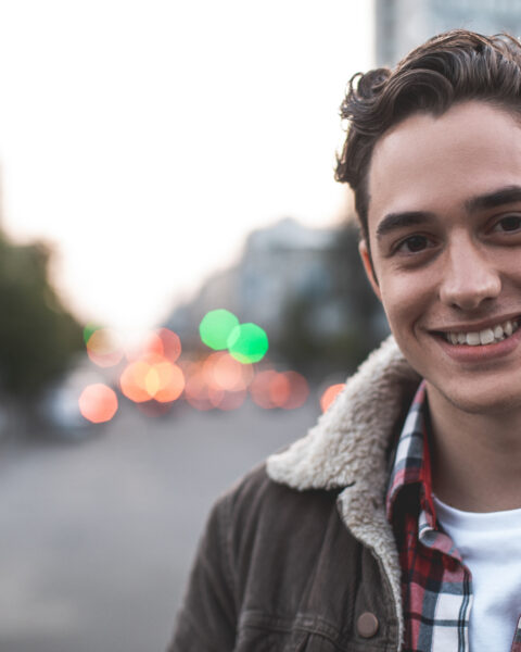 Waist up portrait of delighted young male standing on street and smiling. He is happy to walk on his own. Copy space in left side