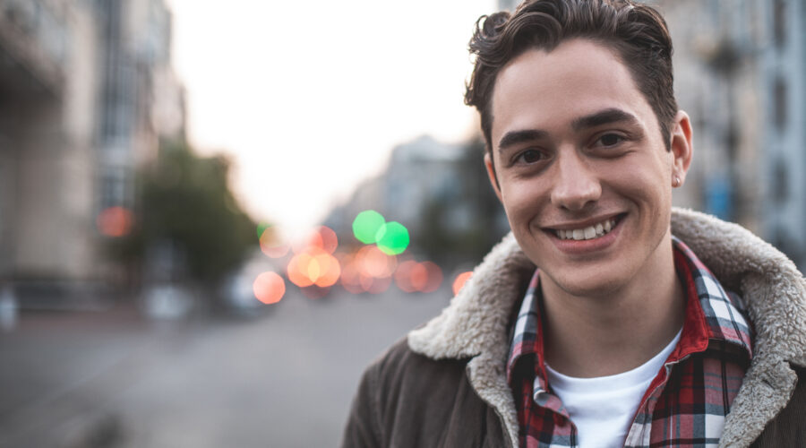 Waist up portrait of delighted young male standing on street and smiling. He is happy to walk on his own. Copy space in left side