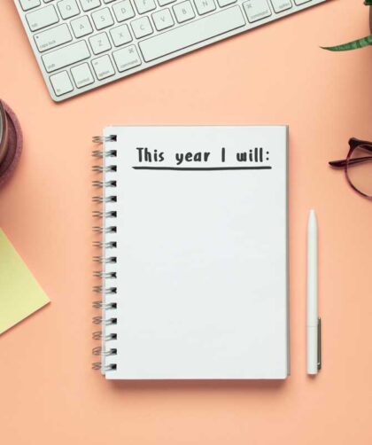 new year notebook with list of resolutions and objects on pink background