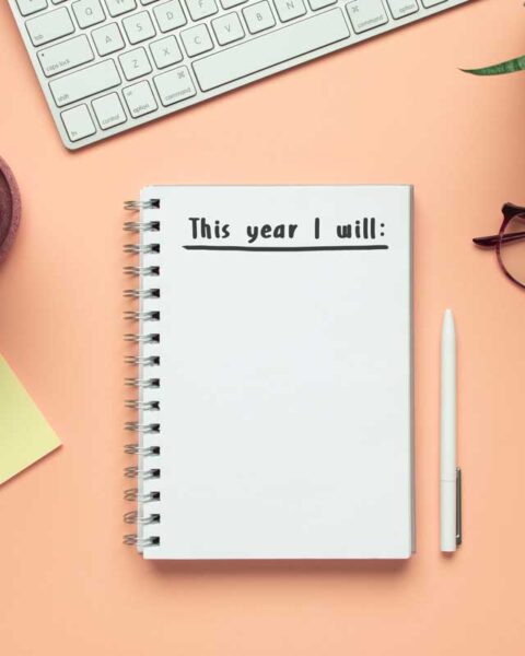 new year notebook with list of resolutions and objects on pink background