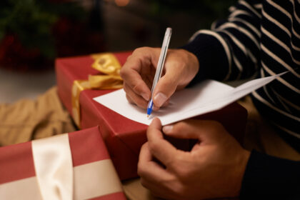 Pen, hands and man with card and gift for Christmas event or party at home for family. Celebration, paper and closeup of male person writing letter with present boxes for xmas festive holiday