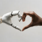 A white ai robot hand and a black human hand come together to form the shape of a heart. Heart shaped by human and ai robot hands. Isolated on light grey background.