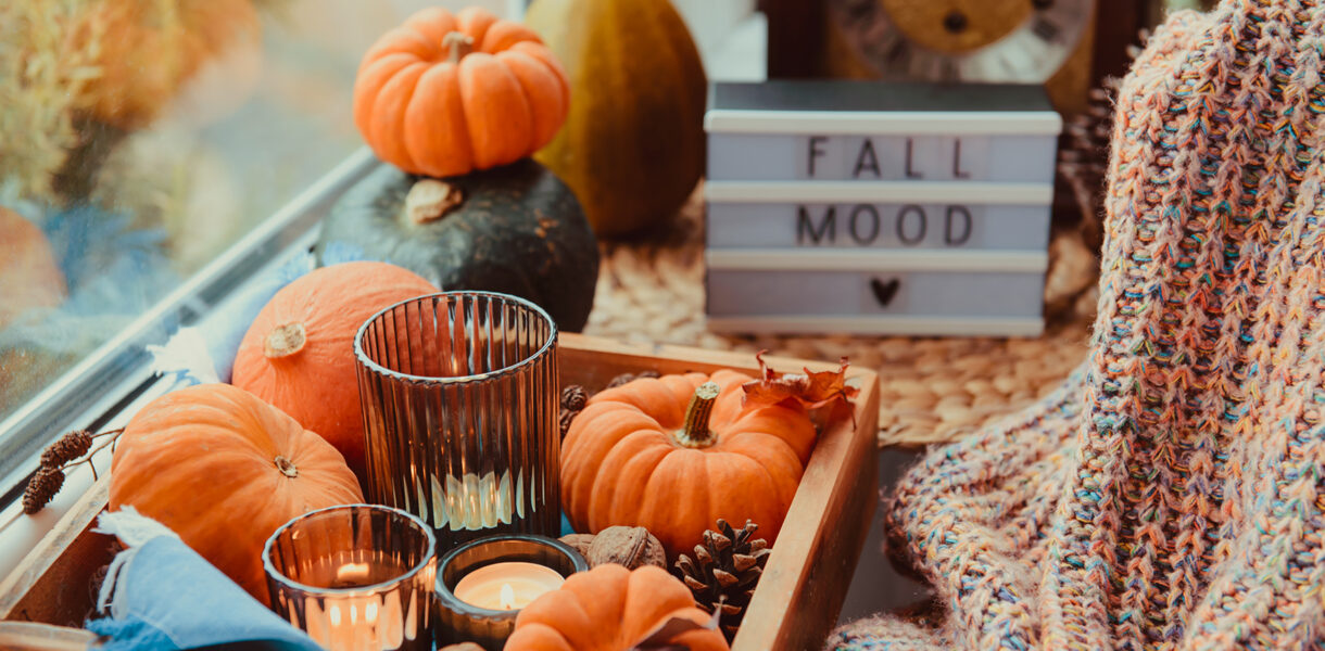 Autumn cozy mood composition on the windowsill. Pumpkins, cones, candles on wooden tray, blurred Fall mood message on lightbox, warm plaid. Autumn, fall, hygge home decor. Selective focus. Copy space