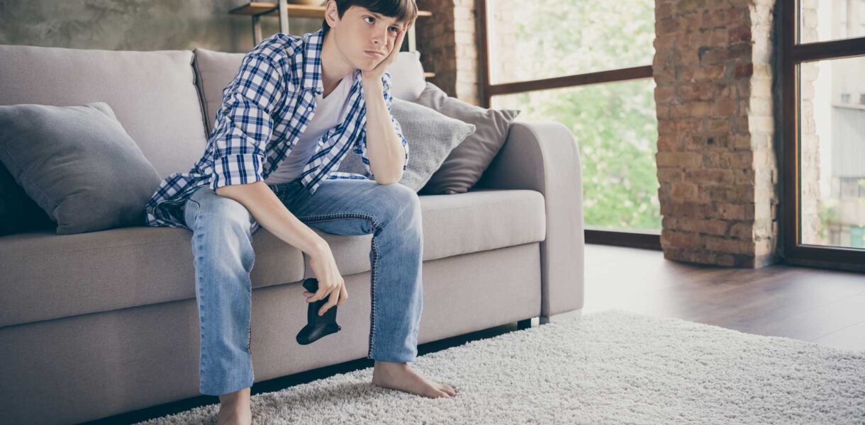 young male sitting on couch with video game control... holding head with hand looking very bored