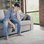 young male sitting on couch with video game control... holding head with hand looking very bored