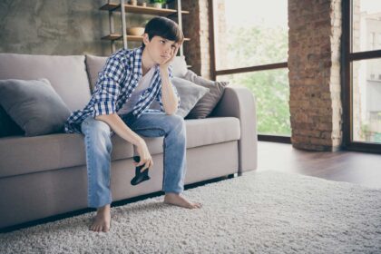 young male sitting on couch with video game control... holding head with hand looking very bored